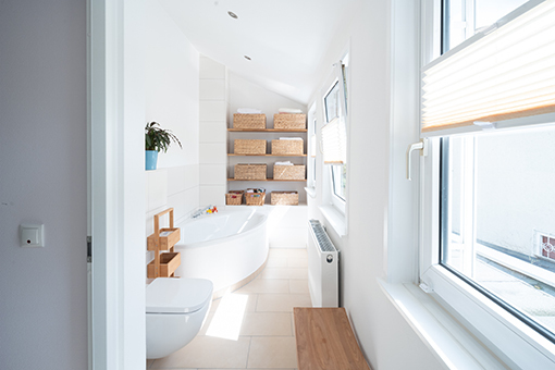 Modernes, helles Bad mit Eckbadewanne, Fenster, Regalen und geflochtenen Körben.
