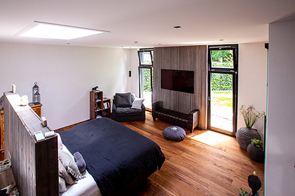 Modernes Schlafzimmer mit Holzboden, großen Fenstern, gemütlicher Sitzecke und Dekoration.