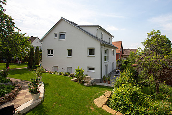 Modernes Einfamilienhaus mit weißer Fassade, großem Garten und gepflegtem Rasen.