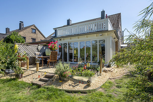 Modernes Einfamilienhaus mit Wintergarten, Terrasse und gepflegtem Garten im Sommer.