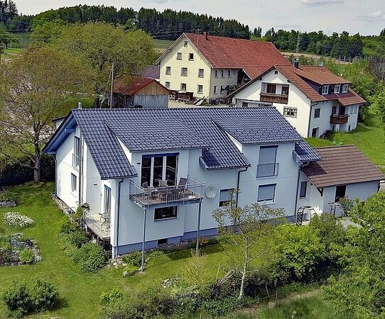 Modernes Einfamilienhaus mit Garten in ländlicher Umgebung und benachbarten Wohnhäusern.
