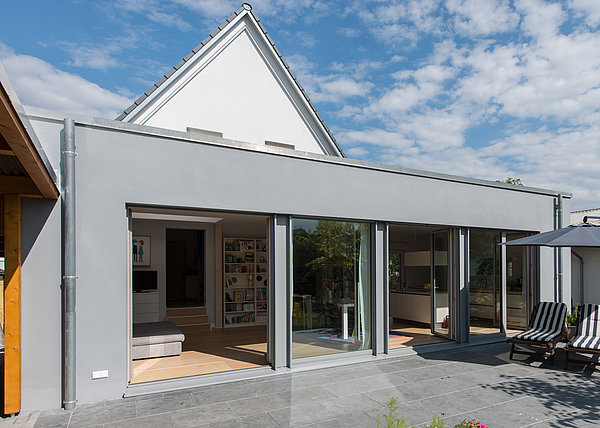 Modernes Einfamilienhaus mit großer Terrasse, bodentiefen Fenstern und Flachdachanbau.